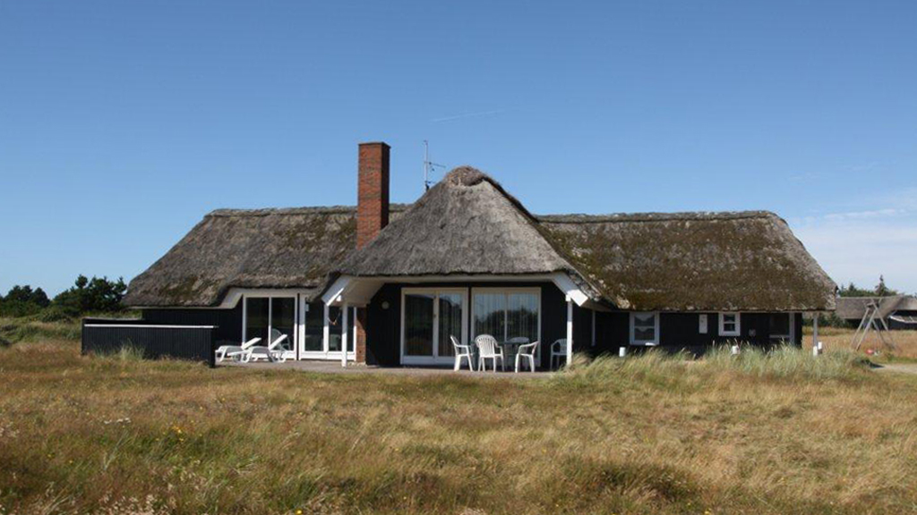 Sort stråtagshus omgivet af marehalm