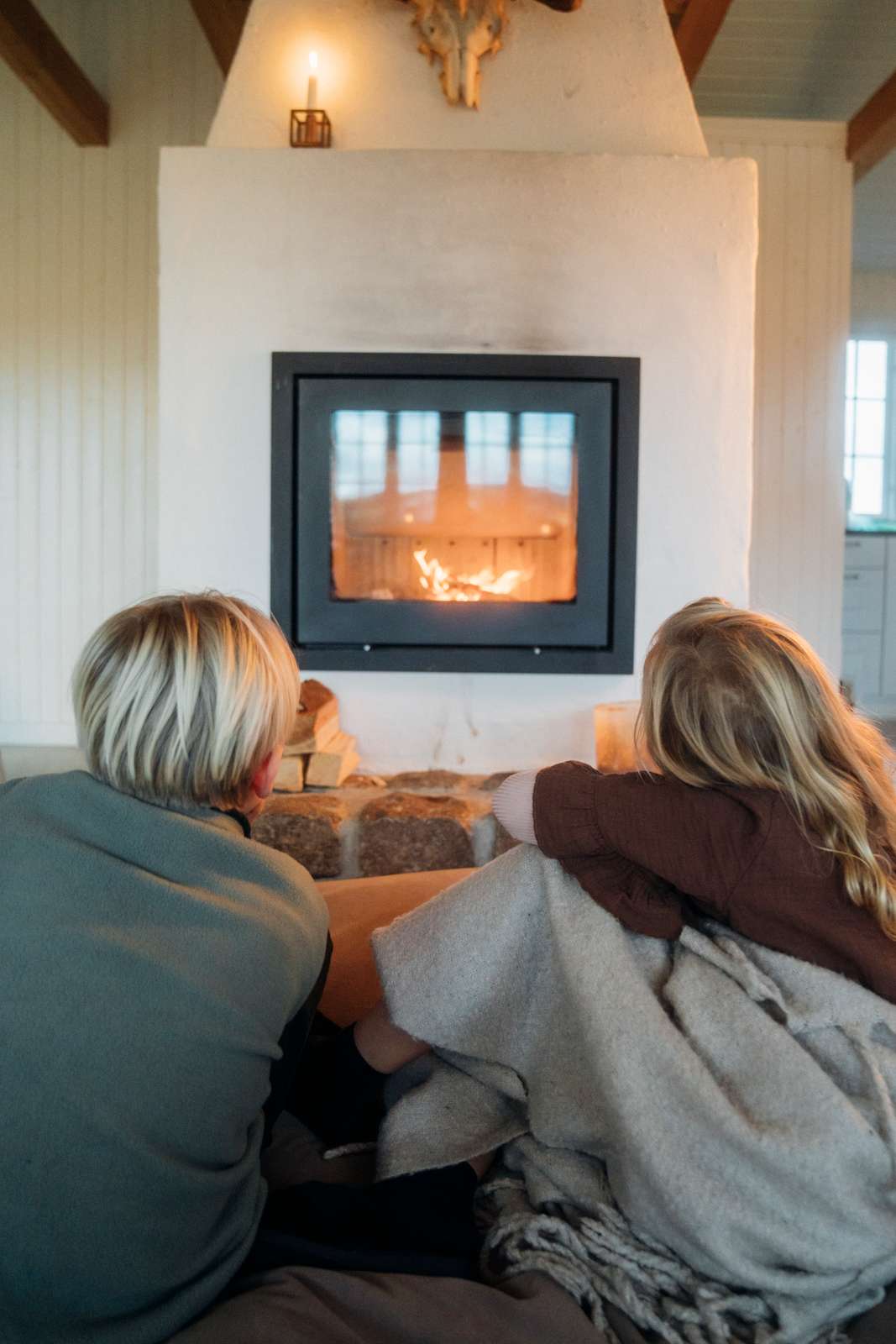 To børn sidder i sommerhus og kigger ind i pejsen om vinteren