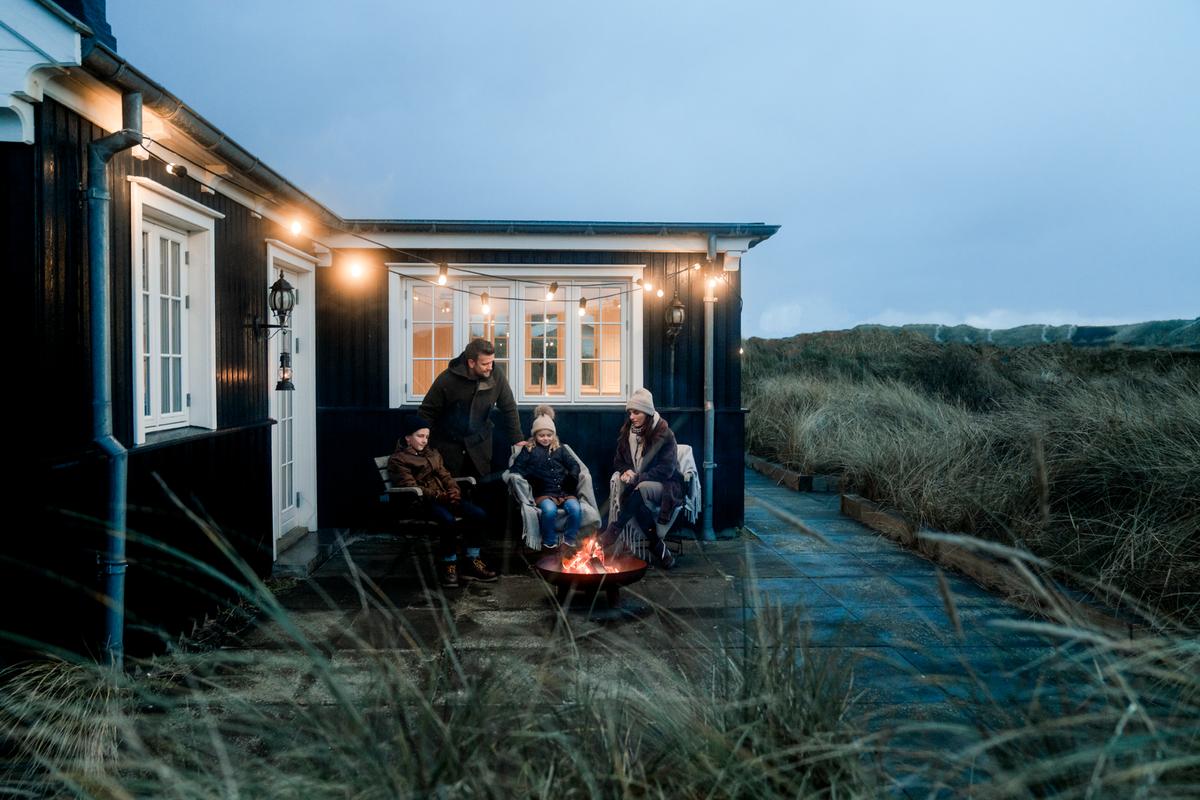 Familie sidder ved bål udenfor sommerhus